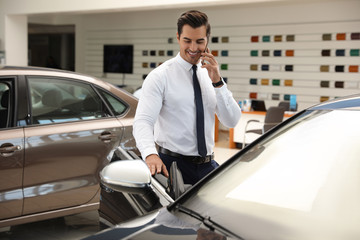Young man talking on phone near car in modern dealership