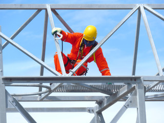 Man Working on the Working at height. Professional industrial climber in helmet and uniform works at height. Risky extreme job. Industrial climbing at construction site.   