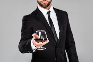 cropped view of successful businessman in black suit holding glass with whiskey isolated on grey