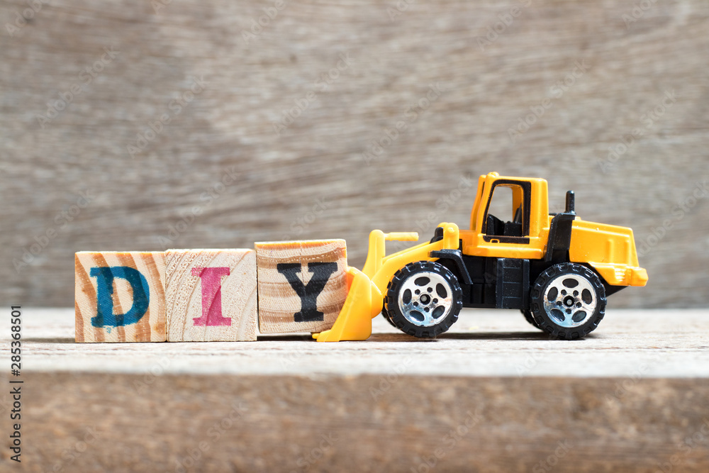 Poster Toy bulldozer hold letter block Y to complete word DIY (abbreviation of do it yourself)  on wood background