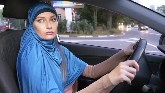 beautiful muslim woman in blue hijab driving a car. rides during the day on the streets of the city.