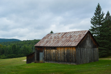Fototapeta na wymiar Weather-worn cedar barn overlooking the landscape in the Adirondack Mountains under a troubled sky