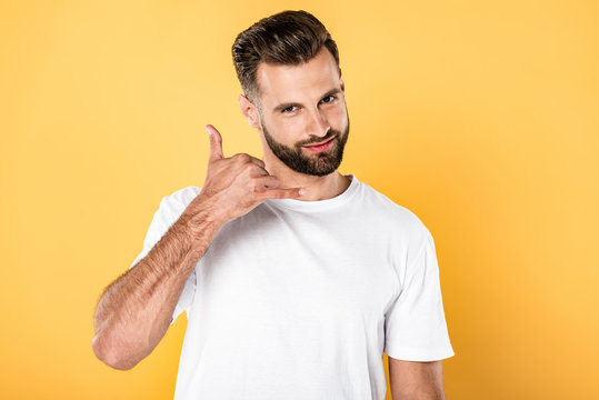 smiling handsome man in white t-shirt showing call me gesture isolated on yellow