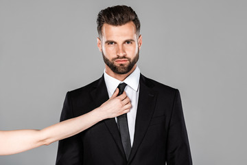 woman touching tie on handsome businessman in black suit isolated on grey