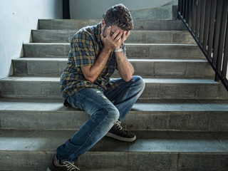 dramatic lifestyle portrait of young depressed and sad man sitting outdoors on dark street...