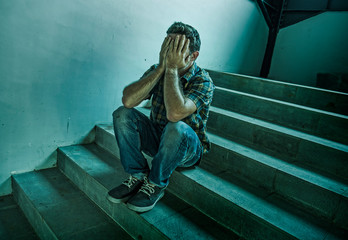 dramatic lifestyle portrait of young depressed and sad man sitting outdoors on dark street staircase suffering depression problem and anxiety crisis crying desperate