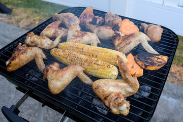 Summer barbecue cooking over a hot fire with chicken wings, drumsticks and corn outdoors