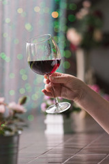 Hand sommelier holding glass of red wine. Glass of red wine on background of colorful bar. Bokeh. Cold toning. Space for text. Concept alcoholic drinks. 