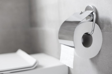 Roll of white toilet paper hanging on metal toilet-paper holder at restroom
