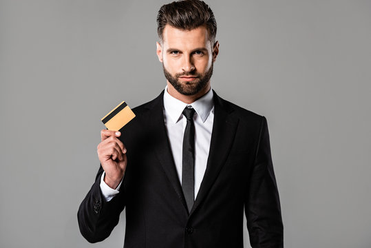 handsome bearded businessman in black suit holding credit card isolated on grey