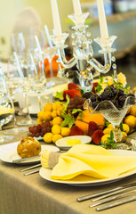 Party dinner table setting with tableware and silverware and glasses set and Candlestick and flower in restaurant.