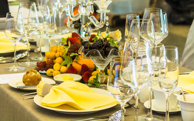 Party dinner table setting with tableware and silverware and glasses set and Candlestick and flower in restaurant.