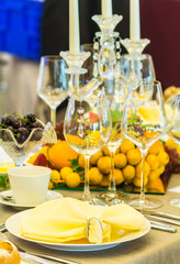 Party dinner table setting with tableware and silverware and glasses set and Candlestick and flower in restaurant.