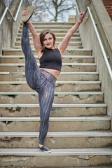 Beautiful young woman poses in athletic wear in urban setting - gymnastics or cheer - stretching leg into heel stretch
