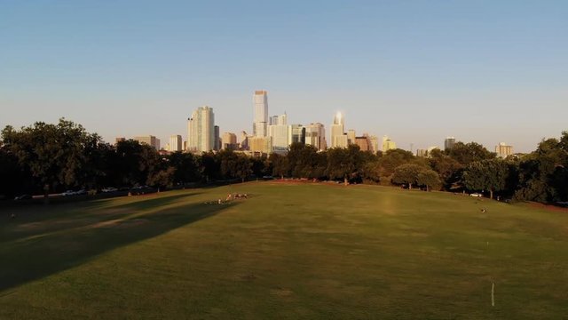 Aerial Drone shot from Zilker Park, going towards downtown Austin, Texas. People in zilker park playing soccer, doing yoga, and being active with their dogs.