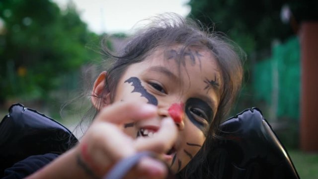 Asian little girl with a painted face is posing facial expression and walking alone in halloween. The children in demon costumes to celebrating halloween. Kids trick or treat. Slow motion.