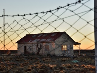 vista de antigua casa abandonada en la meseta patagonica al atardecer a traves del alambrado