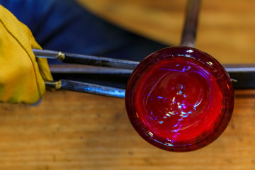 Glass blower shaping a bubble of melted glass on a rod by hand at a glass maker's workshop, shallow depth of field