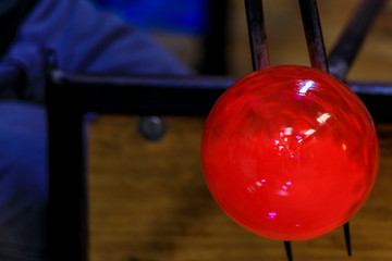 Glass blower shaping a bubble of melted glass on a rod by hand at a glass maker's workshop, shallow depth of field