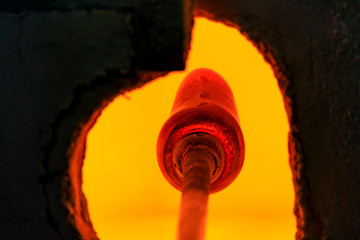 Glass blower working on a bubble of melted glass on a rod by heating it up in a kiln at a glass maker's workshop
