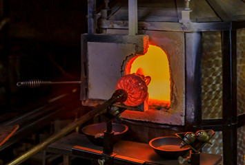 Glass blower working on a bubble of melted glass on a rod by heating it up in a kiln at a glass maker's workshop
