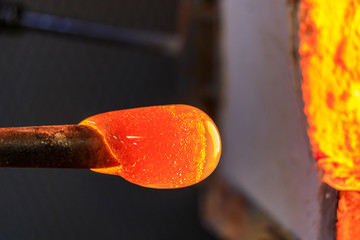 Glass blower working on a bubble of melted glass on a rod by heating it up in a kiln at a glass maker's workshop