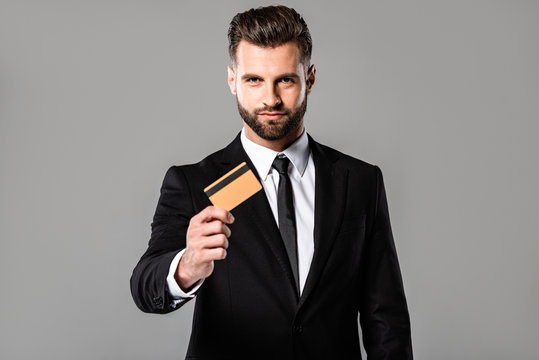 handsome businessman in black suit presenting credit card isolated on grey