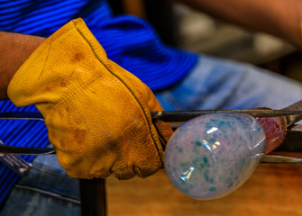 Glass blower shaping a bubble of melted glass on a rod by hand at a glass maker's workshop, shallow depth of field