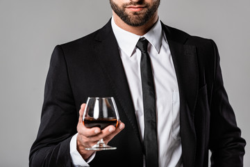 cropped view of bearded businessman in black suit holding glass with whiskey isolated on grey