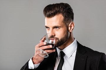 handsome businessman in black suit tasting whiskey isolated on grey