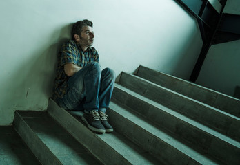 dramatic portrait of young depressed and paranoid man sitting outdoors on dark grunge street corner staircase feeling sick suffering depression problem and anxiety crisis