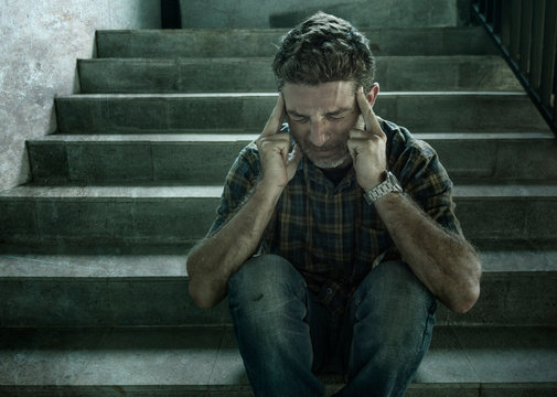 dramatic portrait of young depressed and paranoid man sitting outdoors on dark grunge street corner staircase feeling sick suffering depression problem and anxiety crisis