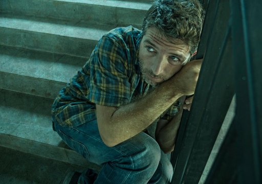 dramatic portrait of young depressed and paranoid man sitting outdoors on dark grunge street corner staircase feeling sick suffering depression problem and anxiety crisis