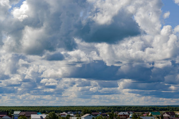 Gray with white storm clouds in the sky over the roofs of houses in the city, beautiful summer landscape, background