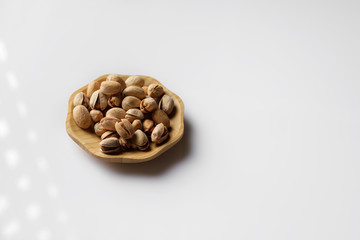 wood plate of salted pistachio nuts isolated on white background.