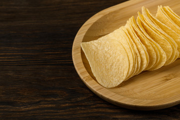 Salty delicious potato chips on wood background. top view
