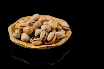 wooden plate of salted pistachio nuts on black background.