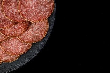 Plate with delicious sliced salami sausage on black board. copy space. top view