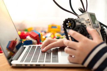 Closeup : hands of preteen / teenage boy codes blocks Mindstorms on his computer laptop, other hand holds robot build for school project. STEM Education, Programming, Robotic Technology, Online Learning