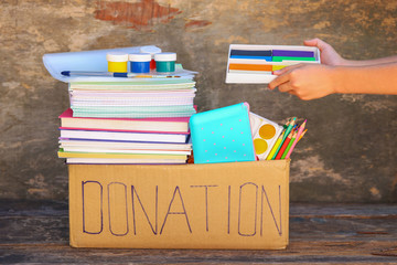 Donation box with school supplies on old wooden background.
