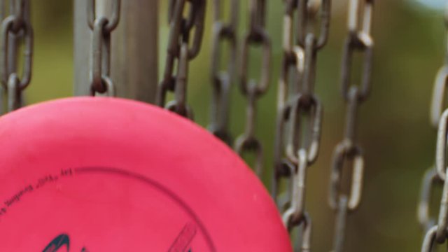 Disc golf disc hits basket chains and falls in, slow motion, closeup