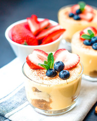homemade, exquisite dessert tiramisu in glasses decorated with strawberry, blueberry, mint on black wooden table