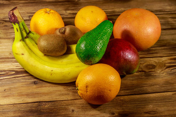 Assortment of tropical fruits on wooden table. Still life with bananas, mango, oranges, avocado, grapefruit and kiwi fruits