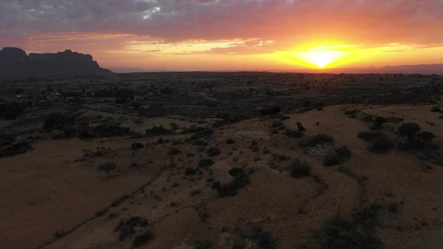 Flying backwards over mountain valley and agricultural fields in deserts of Tigray region at sunset, natural landscapes in Ethiopia