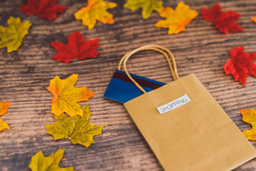 shopping bag with payment card on wooden table surrounded by autumn leaves