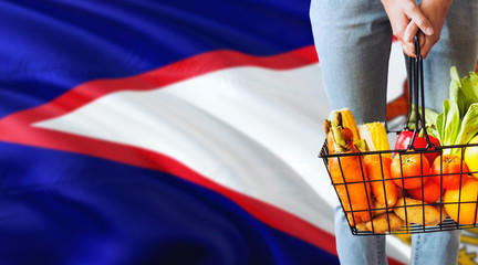 Woman is holding supermarket basket, American Samoa waving flag background. Economy concept for fresh fruits and vegetables.