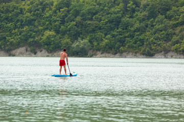 Naklejka premium A young guy is floating on a Board La sup surfing on the lake.