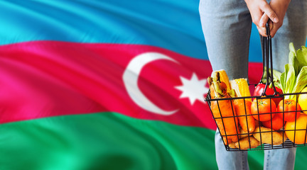 Woman is holding supermarket basket, Azerbaijan waving flag background. Economy concept for fresh fruits and vegetables.