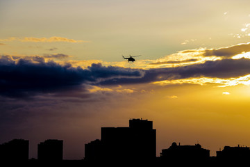A helicopter flies over the city in the evening during sunset.