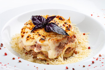 Traditional lasagna made with minced beef bolognese sauce topped with coriander leafs served on a white plate